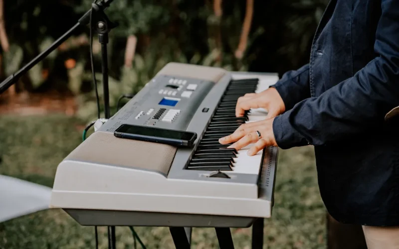 Händer spelar på ett MIDI-piano med en telefon uppställd bredvid